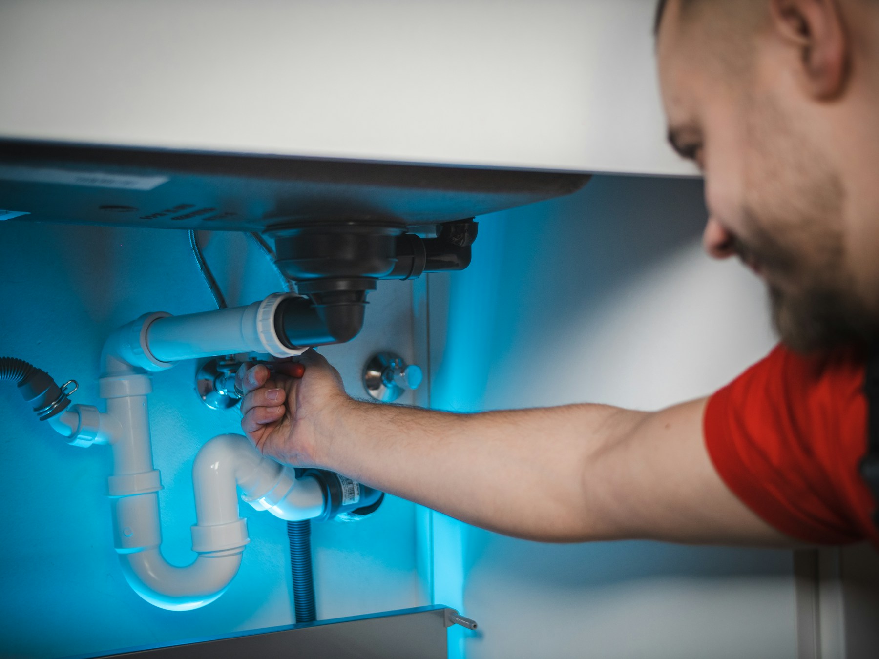 Plumber repairing pipework beneath a sink